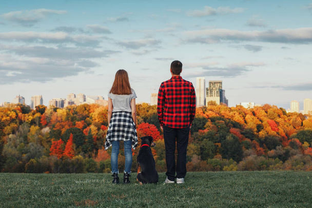 Man, woman and dog pet standing on hill in front of city urban town dreaming of future or remembering past time. View from back. Family with domestic animal. Concept of dreams or travel.  - Foto, imagen