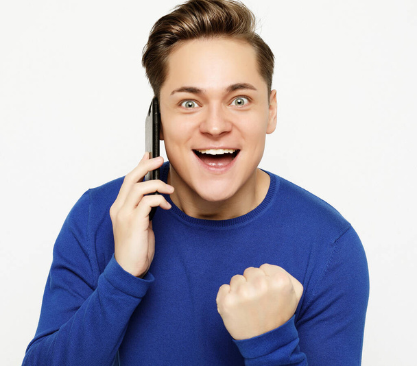 Happy young man in shirt gesturing and smiling while talking on the mobile phone - Foto, Bild