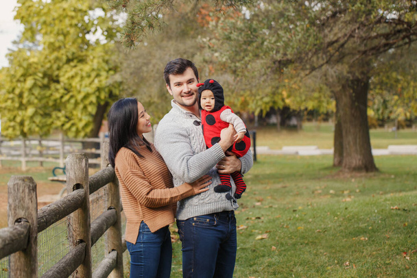 Šťastný usměvavý asijský čínský matka a běloch otec táta s holčičkou v berušce kostým. Rodina v podzimním parku venkovní. Halloween nebo sváteční koncept Díkůvzdání. - Fotografie, Obrázek