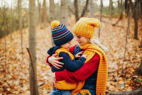 Madre joven caucásica abrazándose hablando con el lindo niño adorable hijo en otoño parque de otoño al aire libre con hojas de árbol rojo anaranjado amarillo. Familia feliz. Actividad estacional otoñal al aire libre
. - Foto, Imagen