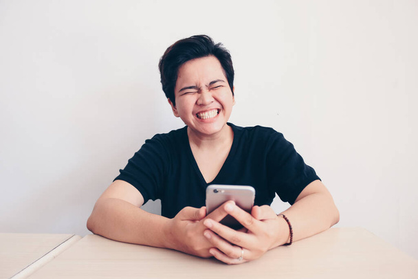 Short hair asian woman holding smart phone in hand, screams with joy and happiness, surprise feeling, winner expression, black shirt, white background. Indonesian women - Foto, Imagem