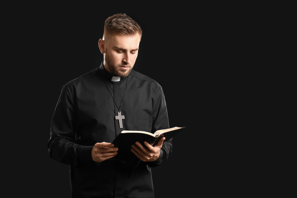 Jonge priester met bijbel op donkere achtergrond - Foto, afbeelding