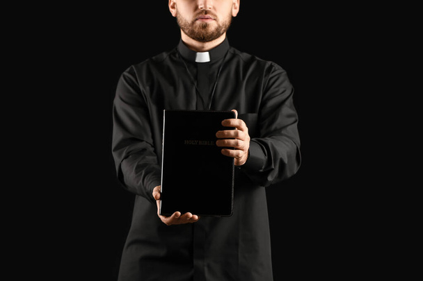 Jonge priester met bijbel op donkere achtergrond - Foto, afbeelding