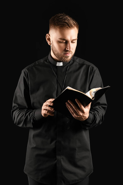 暗闇の中で聖書を持つ若い司祭 - 写真・画像