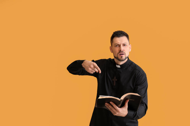 Angry priest with Bible on color background - Photo, Image