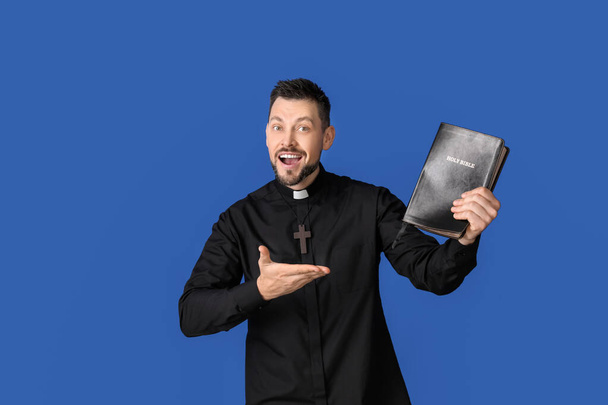 Handsome priest with Bible on color background - Photo, image