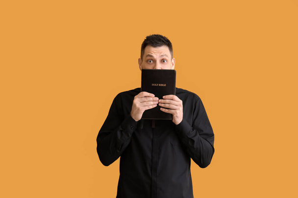 Shocked priest with Bible on color background - Photo, Image