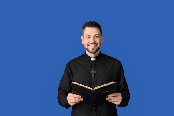 Handsome priest with Bible on color background - Photo, Image