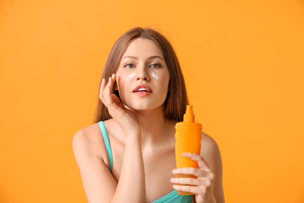 Young woman applying sunscreen cream against color background - Foto, Imagem