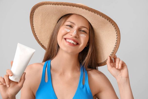 Young woman with sunscreen cream against light background - Foto, afbeelding