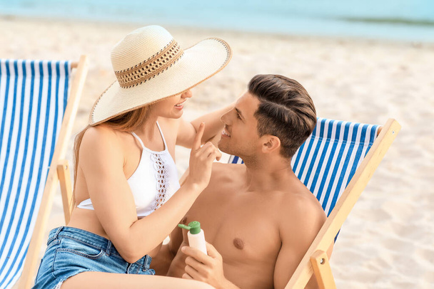 Jeune couple appliquant crème solaire sur la plage de la mer - Photo, image