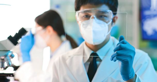 Asian male scientist or microbiologist look the blank virtual display on transparent futuristic tablet pc in the lab - Photo, Image