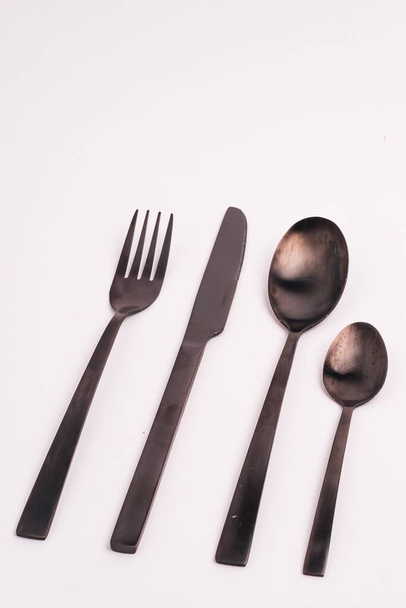 A vertical closeup shot of a knife, fork, and two spoons isolated on a light-colored background - Photo, Image