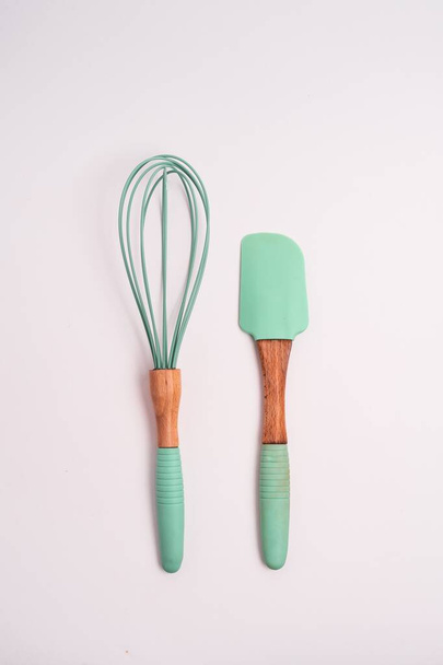 A vertical closeup shot of green kitchen whisk and shovel isolated on a light-colored background - Photo, Image
