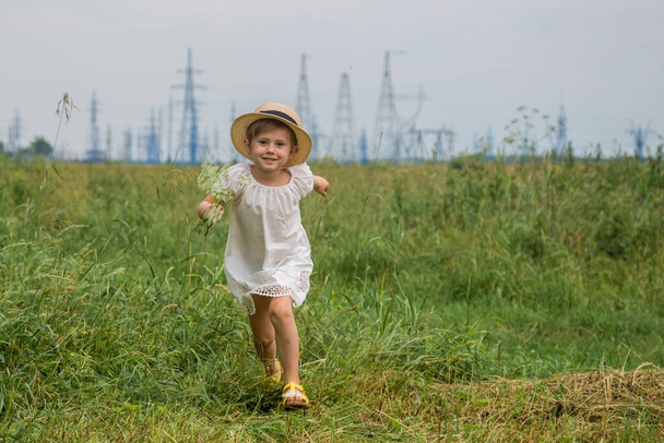 4 years old baby girl in a white boho dress with a hat running in the field - Fotoğraf, Görsel