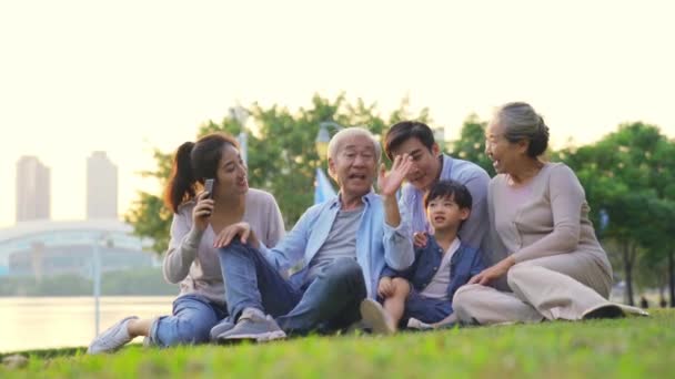 felice tre generazione asiatico famiglia seduta su erba all'aperto prendere un selfie - Filmati, video