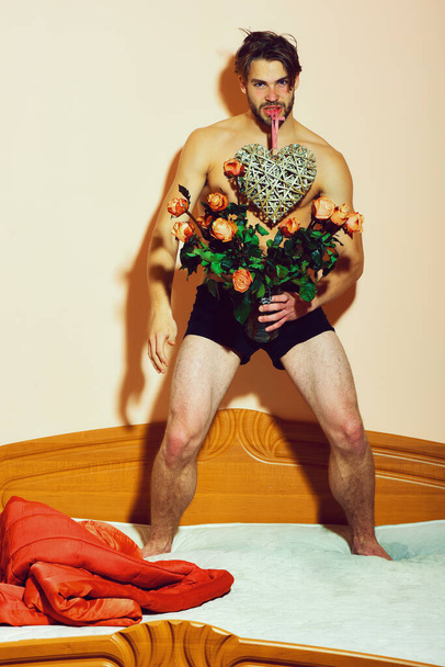 bearded macho man on bed near red blanket holding orange roses - Foto, Imagem