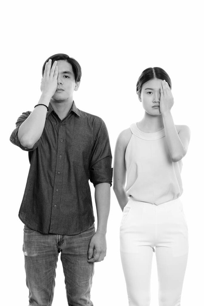 Studio shot of young Asian woman and young Filipino man as couple together against white background in black and white - Fotó, kép