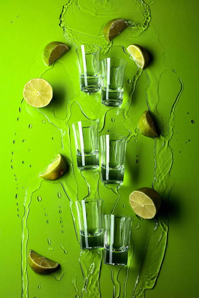 Small shot glasses with lime slices and flowing drink on a green background.  - 写真・画像