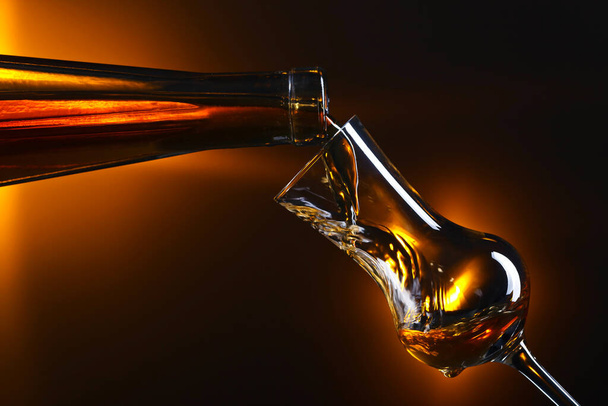 Pouring alcoholic drink into a glass on dark background. - Photo, Image