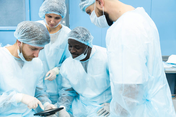 A team of doctors in uniform and medical masks looks at a surgical plan on an electronic tablet - Fotografie, Obrázek