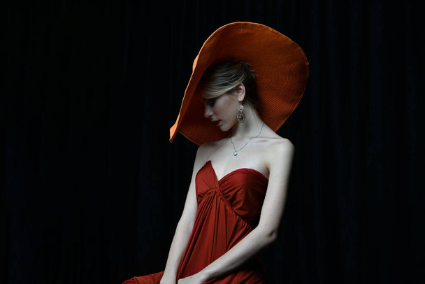 красива дівчина в бордовому капелюсі і в бордовій вечірній сукні позує на чорному тлі
 - Фото, зображення