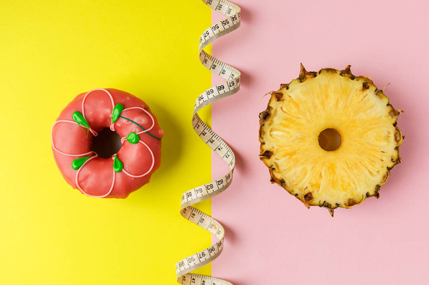 ένα ντόνατ και έναν κύκλο φρέσκου ανανά σε κίτρινο-ροζ φόντο. την έννοια της επιλογής του σωστού τροφίμου. - Φωτογραφία, εικόνα