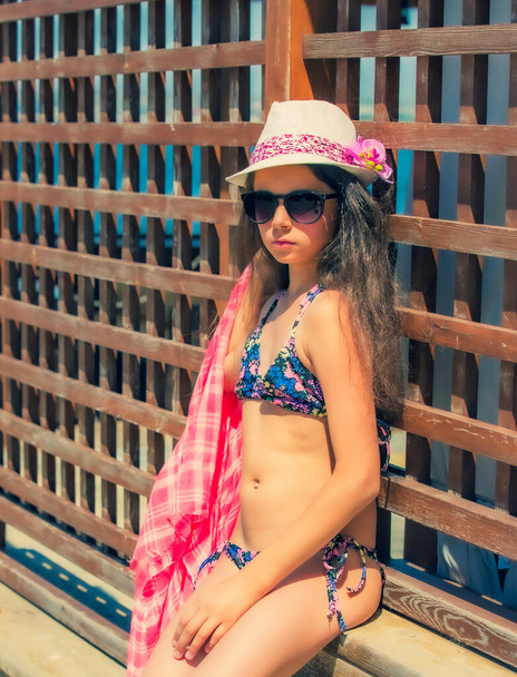 Summertime portrait of young girl in a swimsuit standing by the wooden fence - Photo, image