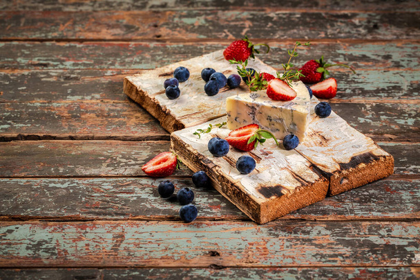 Blue and brie cheese. On a wooden background. served with blueberry and strawberry. The concept of eco products. Background image. Copy space. - Zdjęcie, obraz