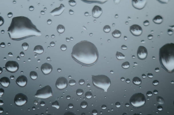 Krople deszczu na powierzchni okularów okiennych z zachmurzonym tłem. Naturalny wzór kropel deszczu wyizolowanych na mętnym tle. - Zdjęcie, obraz