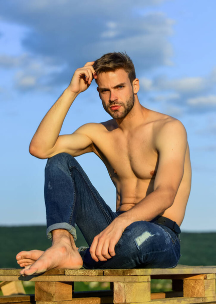 Fitness model. Athletic handsome macho wear denim pants. Muscular body. Muscular bare torso. Six packs muscular chest. Man outdoors blue sky background. Male beauty concept. Summer lookbook - Foto, afbeelding