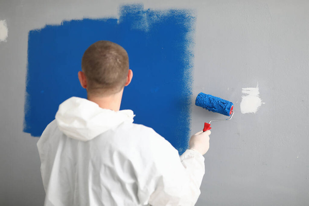 Elinde silindir olan bir adam duvarı maviyle boyuyor.. - Fotoğraf, Görsel