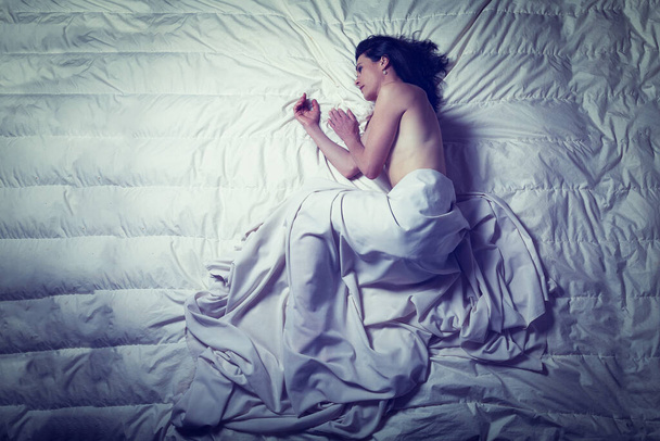 Conceptueel beeld van een vrouw een verdrietig en eenzaam op een bed onder een laken - Foto, afbeelding