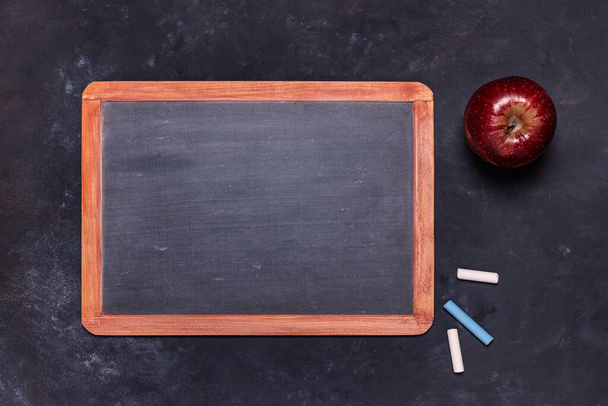 fekete szerkezetű háttérrel, felülnézetből, egy iskolai táblával krétákkal és egy vörös almával. Fénymásolási hely - Fotó, kép