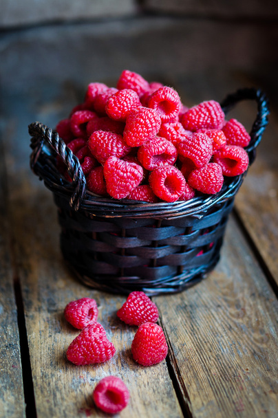 Raspberries in a basket on rustic wooden background - 写真・画像