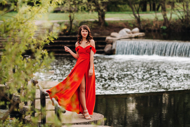 a young beautiful girl with long brown hair, in a long red dress with a ring around the lake. - 写真・画像