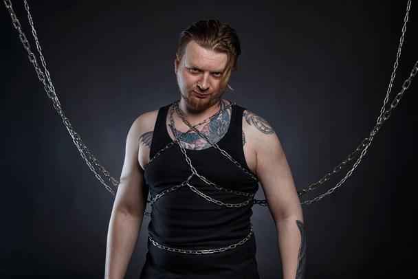 Photo of a tattooed bearded man bound in chains - Foto, Imagen