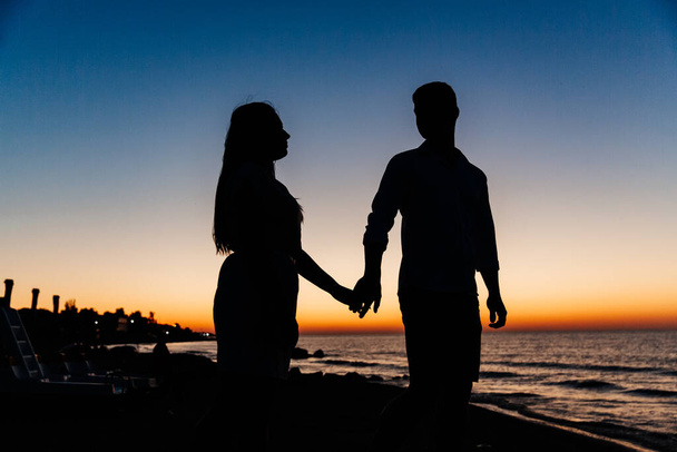Couple amoureux en vêtements blancs lors d'une lune de miel en mer marcher sur le sable lors d'une séance photo Love Story, côte océan, plage - Photo, image