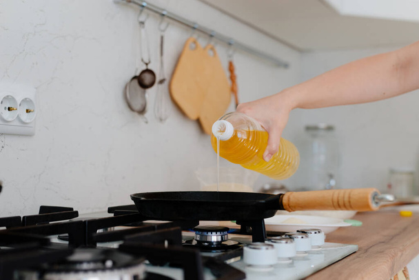 A woman pours oil into a cast-iron pan. Home cooking, a woman pours oil in a pan. - Fotó, kép