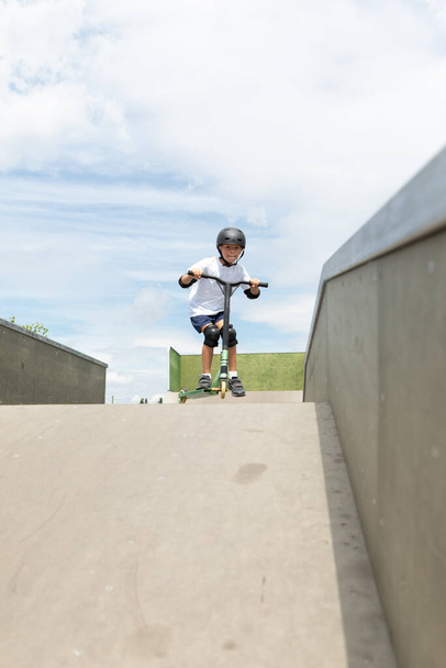 A cute little boy rides a scooter in a skatepark. A young novice athlete spends free time in extreme sports. Lifestyle. - Fotó, kép