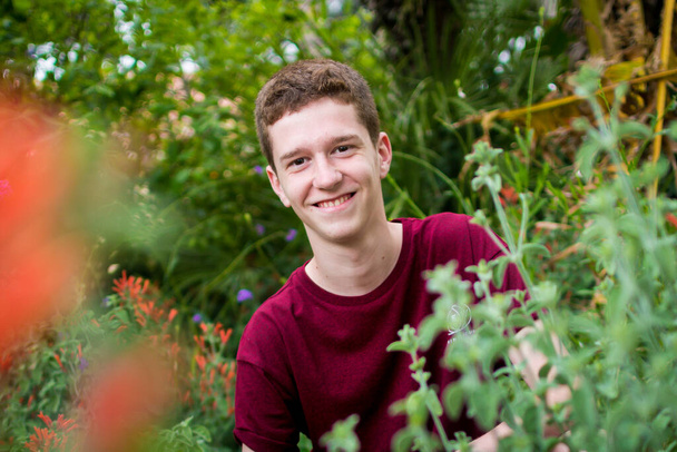 Κοκκινομάλλα έφηβος ψάχνει μεταξύ των φυτών σε ένα μωβ πουκάμισο. - Φωτογραφία, εικόνα