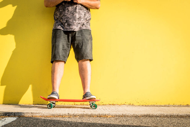 Kurviger Mann mit Skateboard und gelbem Hintergrund beim Blick auf das Smartphone. - Foto, Bild