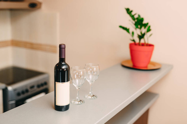 Eine Flasche Wein und zwei leere Gläser auf der Theke in der Küche. - Foto, Bild