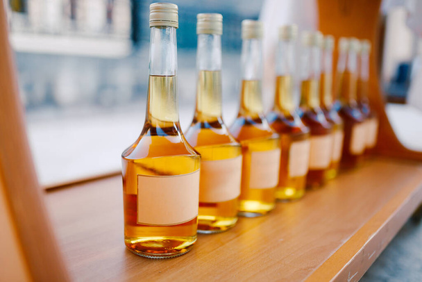 Bottles with a golden alcoholic beverage. Empty labels. Bottles of Rakia are on display in a row. - Foto, Imagen