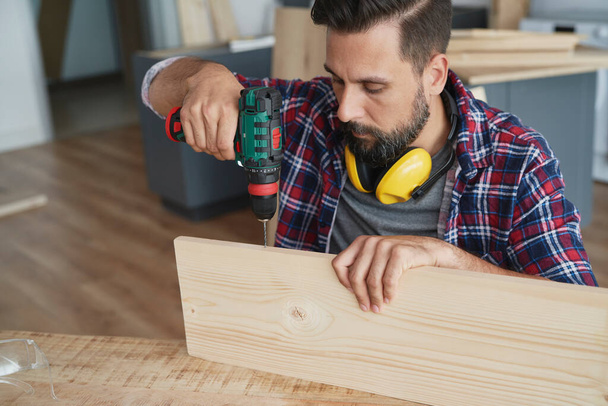 Focused carpenter drilling in a wooden plank                                - Photo, Image