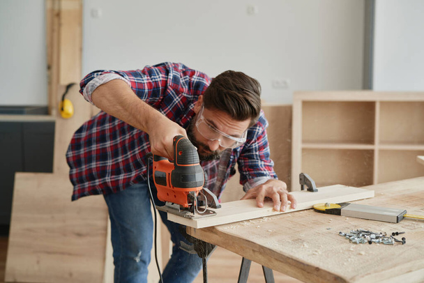 Carpinteiro serrar madeira com um quebra-cabeça elétrico
                                - Foto, Imagem