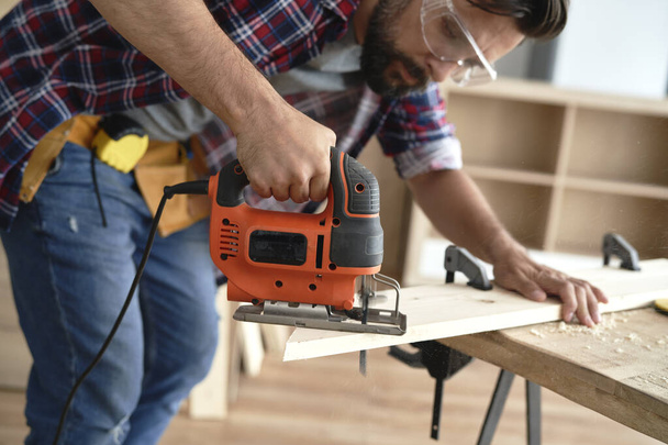 Carpenter using an electric jigsaw to cut wood                                - Foto, Imagen