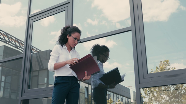 Afrikaans-Amerikaanse zakenvrouw met papieren mappen in de buurt van gebouw op stedelijke straat - Video
