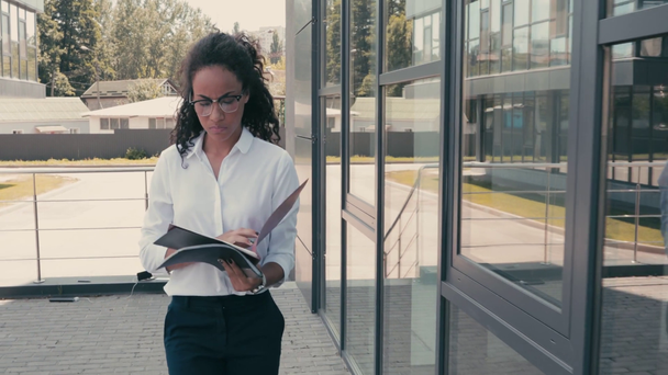 建物の近くを歩く書類を持つアフリカ系アメリカ人の実業家 - 映像、動画