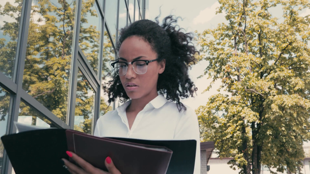 Skeptical african american businesswoman with papers walking on urban street  - Footage, Video